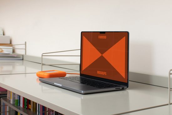 Laptop and orange external hard drive on a minimalist desk with books; perfect for showcasing digital mockups, templates, graphics in creative design projects.