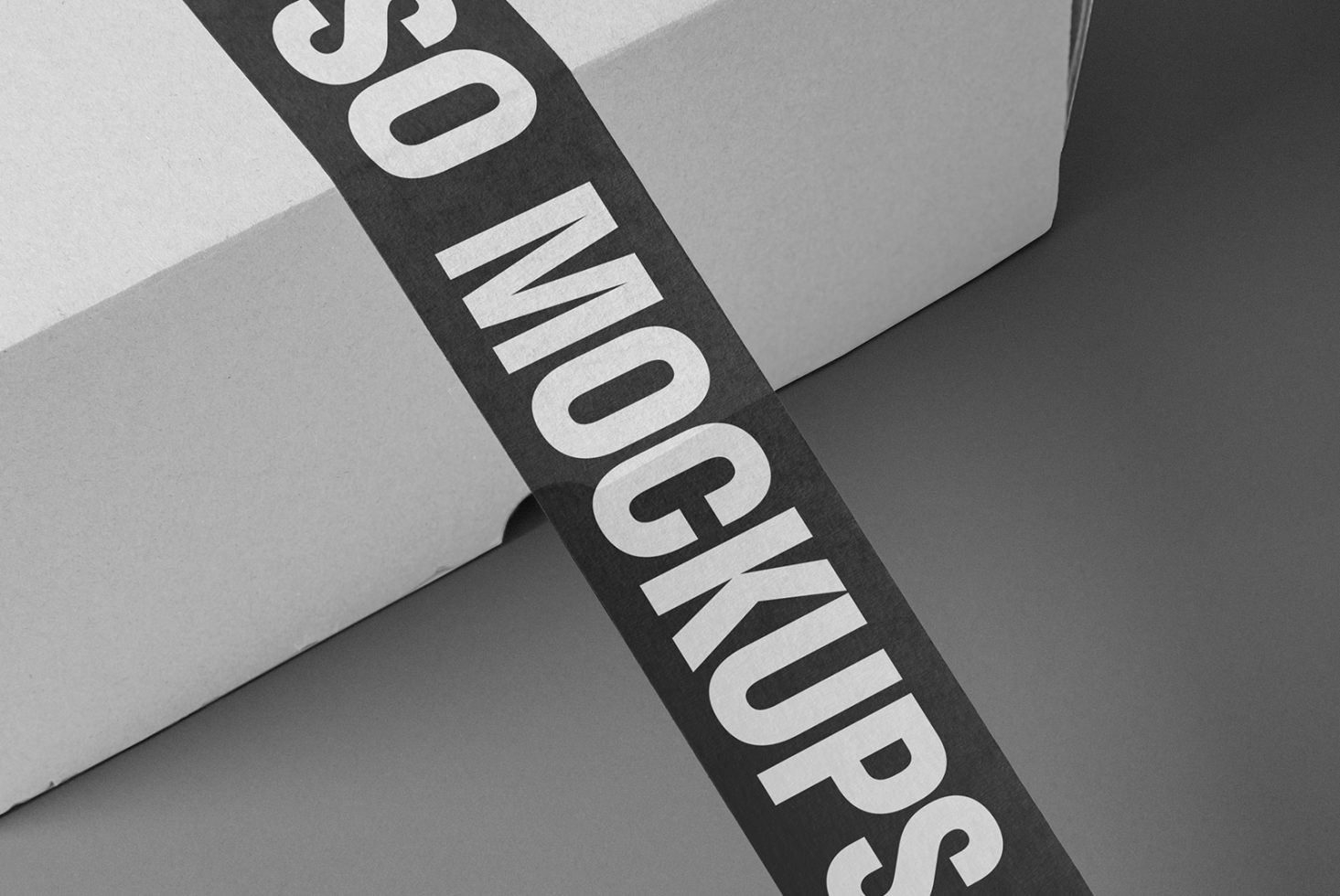 Close-up of a black tape with bold white text saying SO MOCKUPS on a grey cardboard box, ideal for designers seeking high-quality mockup templates.