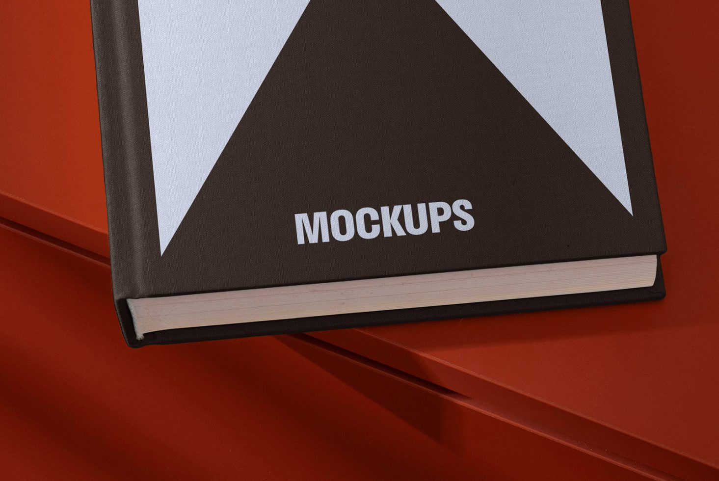 Book cover mockup on red background with a geometric design and the word mockups written on the cover. Suitable for designers. Keywords: book, mockup, design.