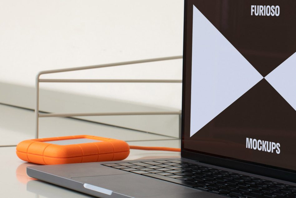 Laptop with external orange hard drive on desk for mockup design showcasing workspace digital assets templates for designers SEO keywords mockups laptop tools