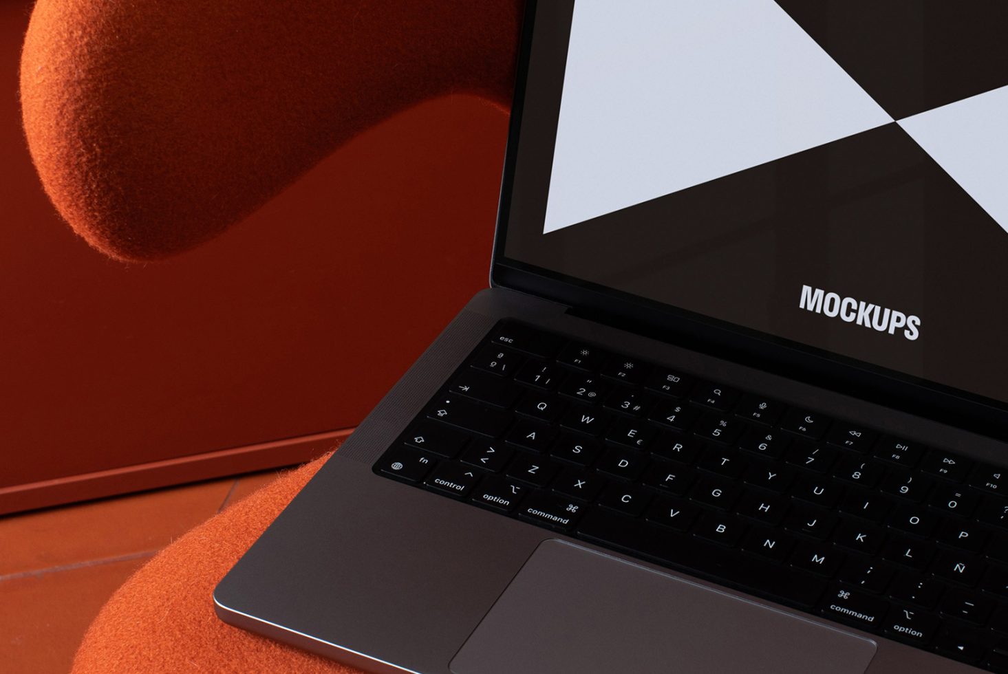 Laptop displaying mockups on screen with a black keyboard, placed on an orange textured chair, suitable for designers digital assets like templates mockups.