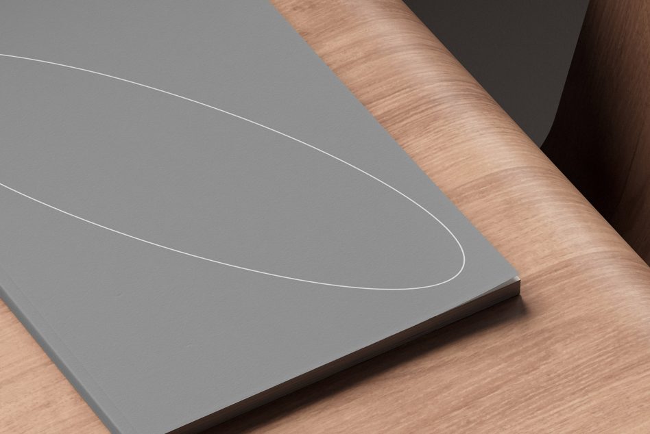 Gray closed notebook with an oval line design placed on a wooden desk. Ideal for mockup presentations, branding projects, and digital assets for designers.