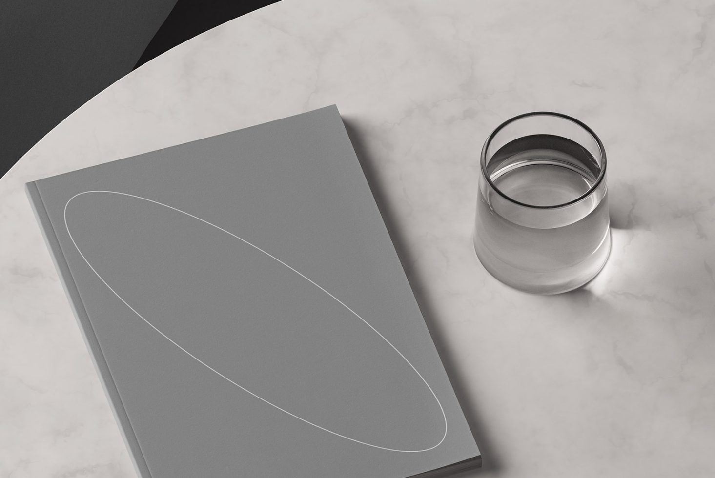 Minimalist Mockup: Grey hardbound book with geometric design next to a glass of water on a marble table. Perfect for graphic designers templates.