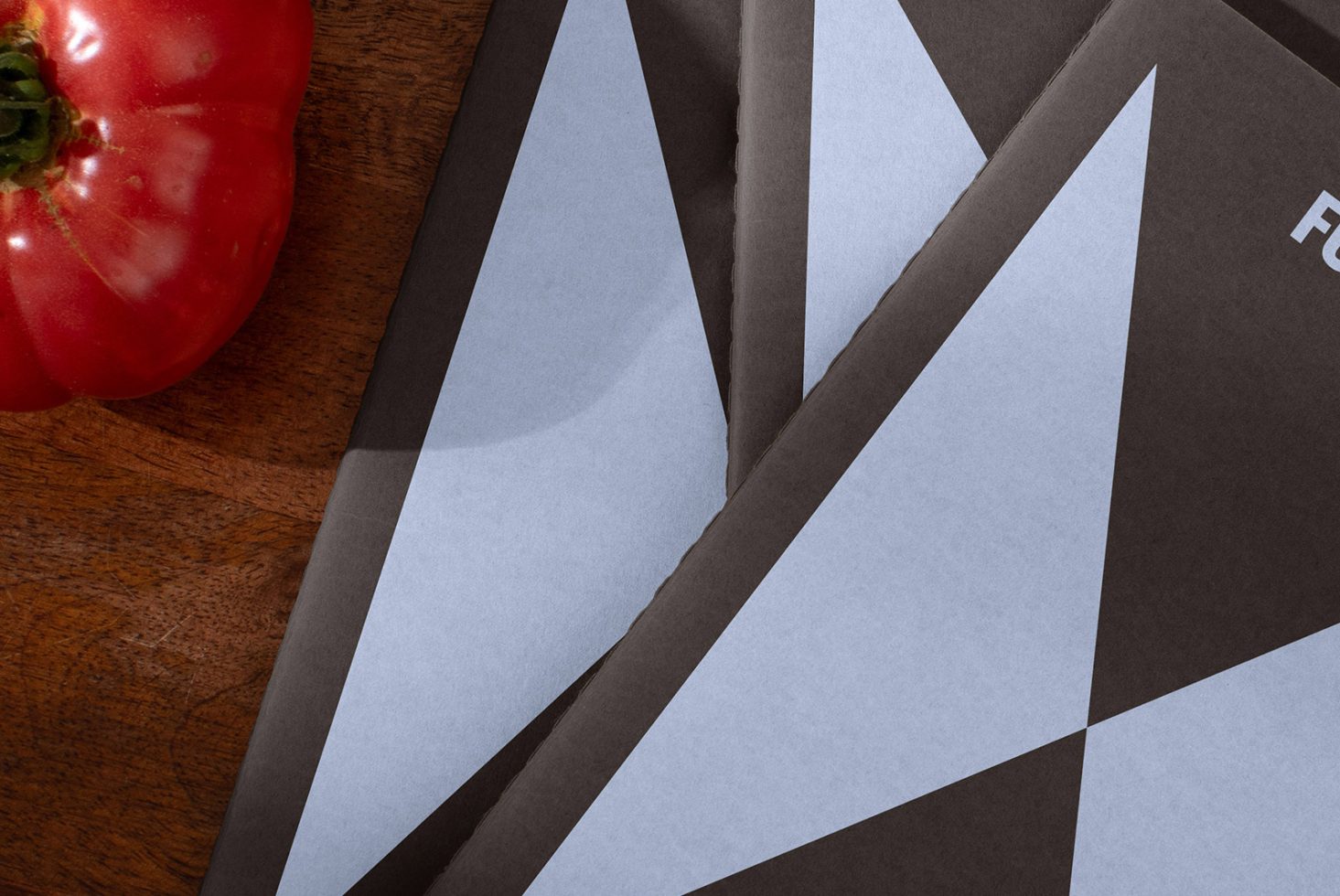 Close-up of geometric patterned templates with triangle designs on wood surface alongside a tomato. Keywords: design templates, geometric, mockups, patterns.