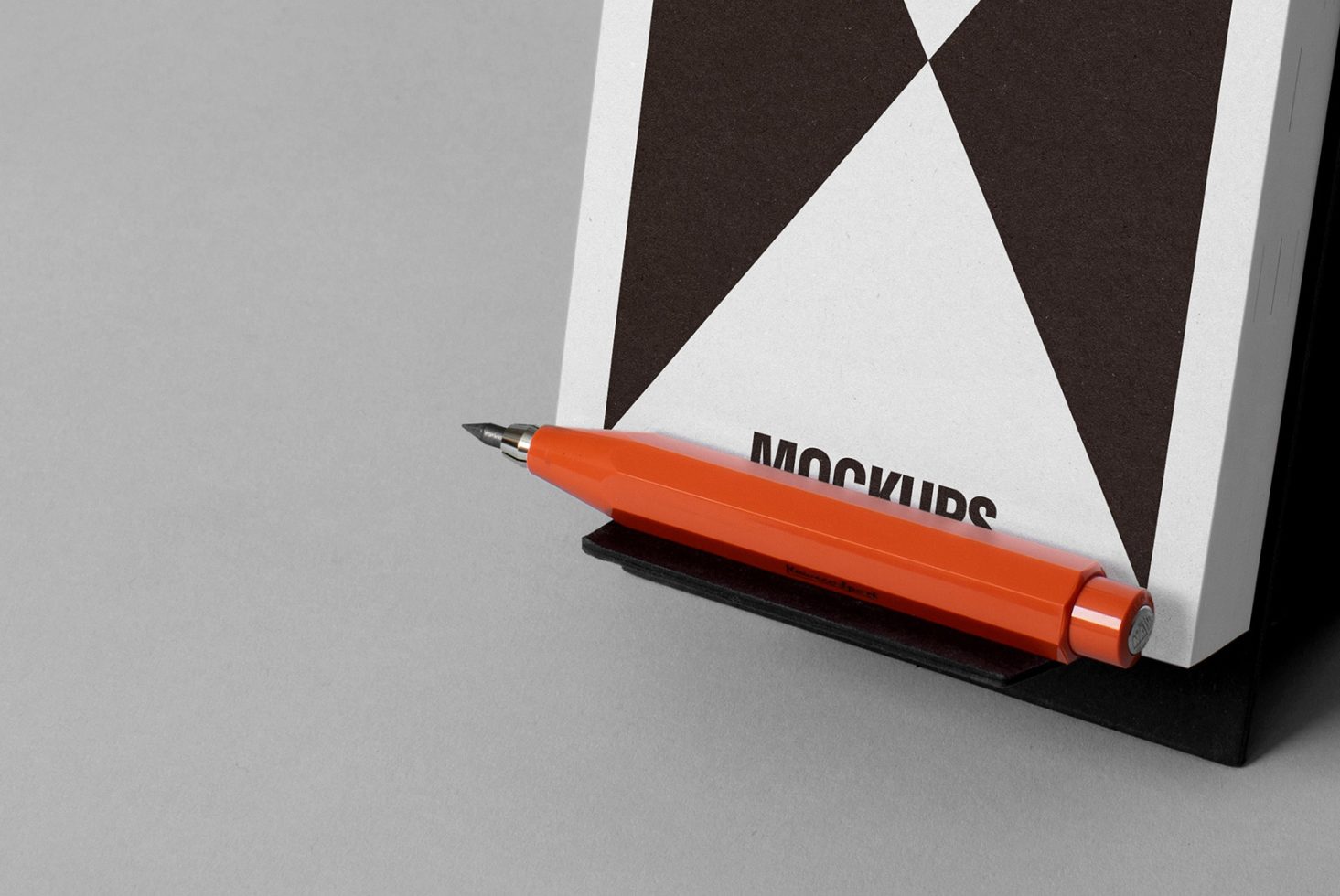 Book mockup with geometric design resting on a stand along with an orange mechanical pencil. Perfect for designers looking for clean and professional presentations.