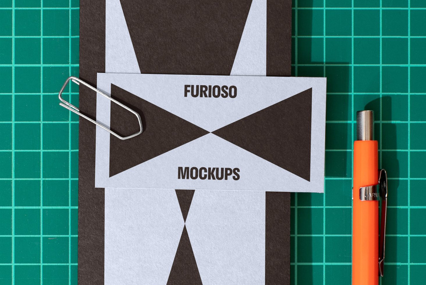 Mockup showcasing business cards with geometric design on green grid background, accompanied by a paperclip and an orange pen. Keywords: mockup business card.