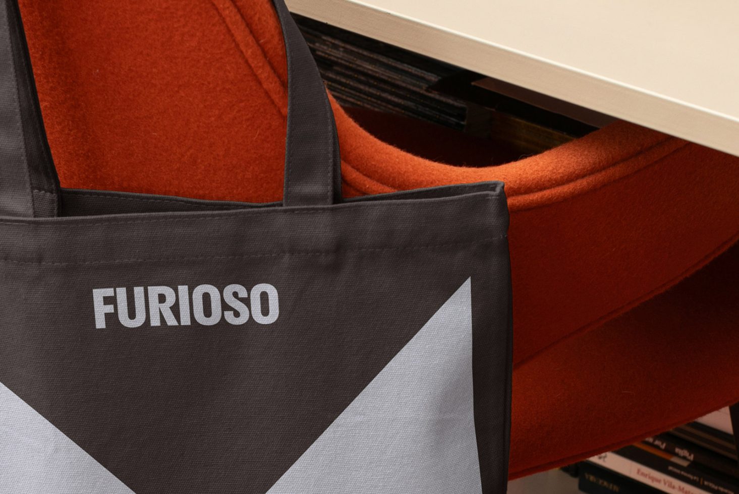 Mockup of a black tote bag branded with the word Furioso, draped over an orange chair, ideal for product presentation and design showcasing.