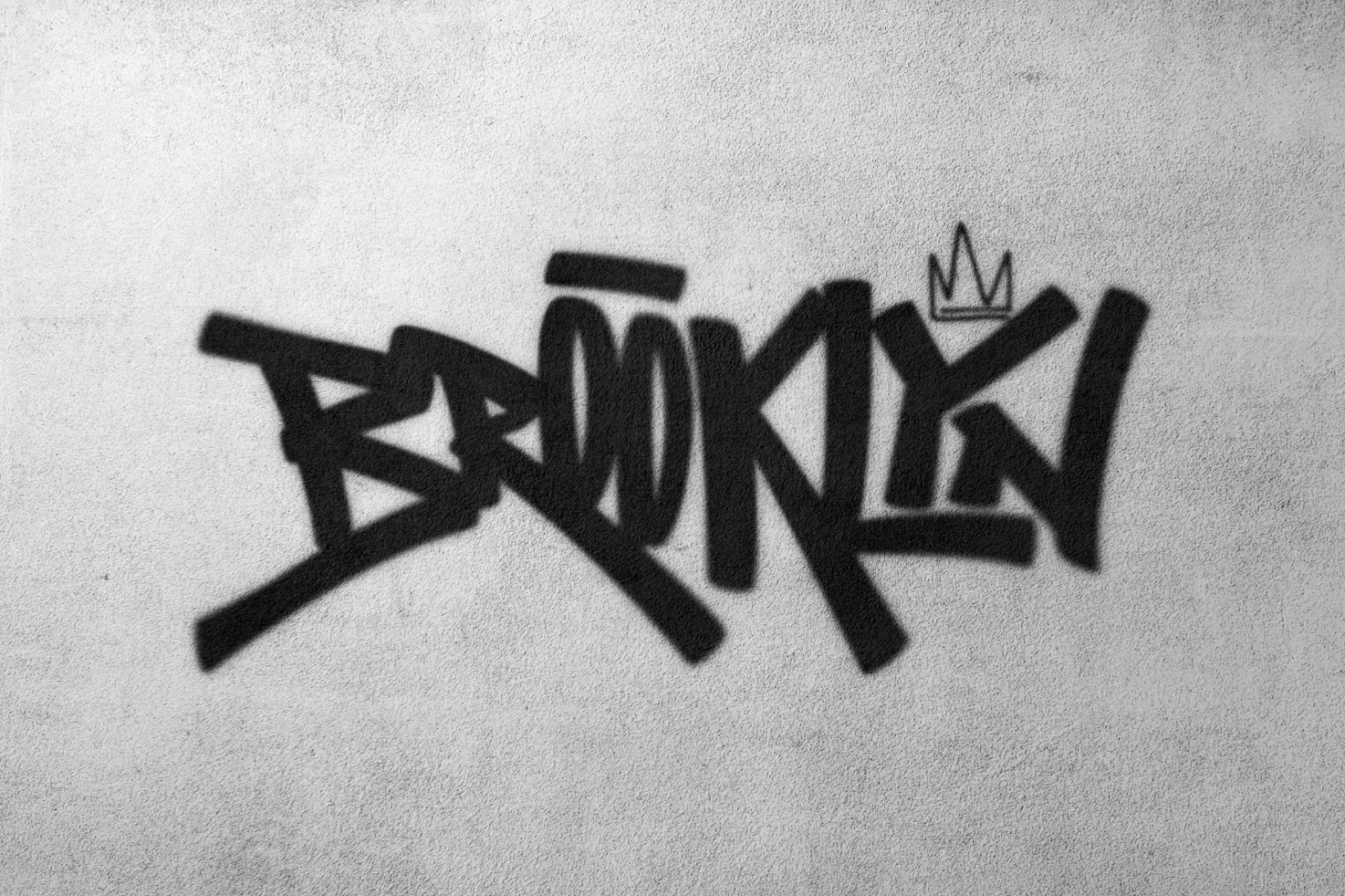 Black graffiti text Brooklyn with a small crown on a beige concrete wall. Perfect for urban fonts, street art graphics and hip-hop mockups.