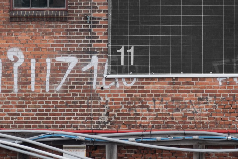 Graffitied brick wall with large white numbers, visible wiring, small window above. Suitable for graphics, texture backgrounds, urban design projects.