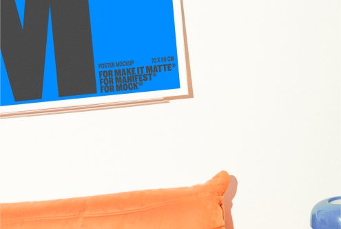 Poster mockup on white wall above orange cushion displays large M and text For Make It Matte For Manifest For Mockup. Suitable for graphic and web designers.