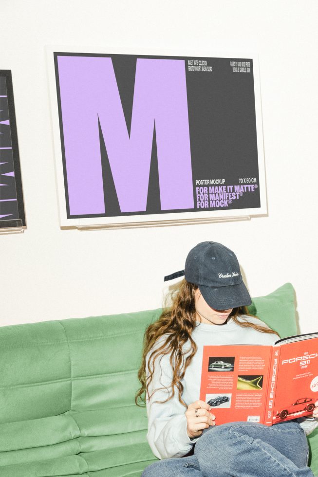 Woman wearing a cap sitting on green couch reading a book with large purple M poster mockup on the wall behind her. Poster Mockup, Design Assets for Designers.