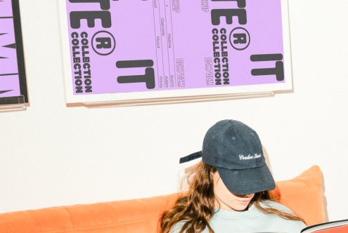 Designer reading a magazine on an orange couch. Posters with bold, black text on a purple background are displayed above. Ideal for templates or graphic design mockups.