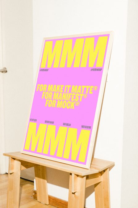 Hot pink poster with neon yellow letters displayed on natural wood stool