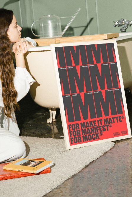 Man seated near bathtub looking at framed A2 poster mockup with bold red and black design INS text. Perfect for designers for templates and graphics assets.