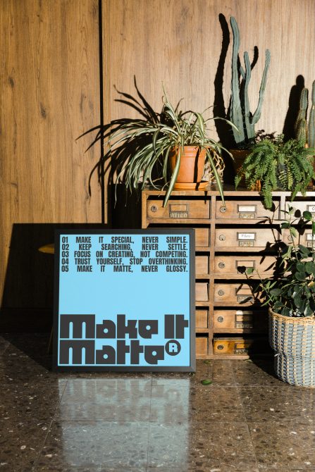 Blue poster with design manifesto leaning against vintage wooden drawer unit with hanging plants