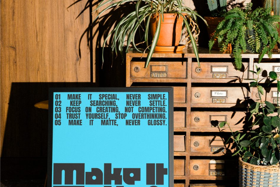Light blue poster with dark text manifesto positioned by vintage wood drawers, potted orange plant, trailing fern