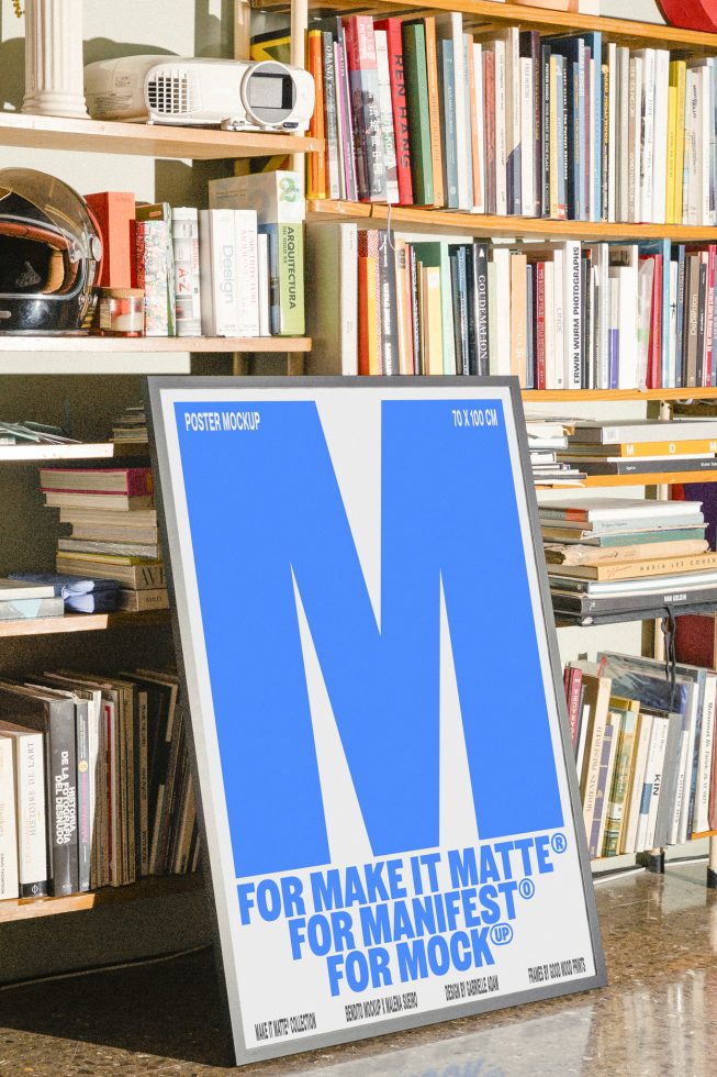 Vertical poster mockup featuring a bold blue M on a white background, placed indoors against a bookshelf filled with design books. Keywords: Poster Mockup, Design Template, Digital Asset, Graphic Tool.