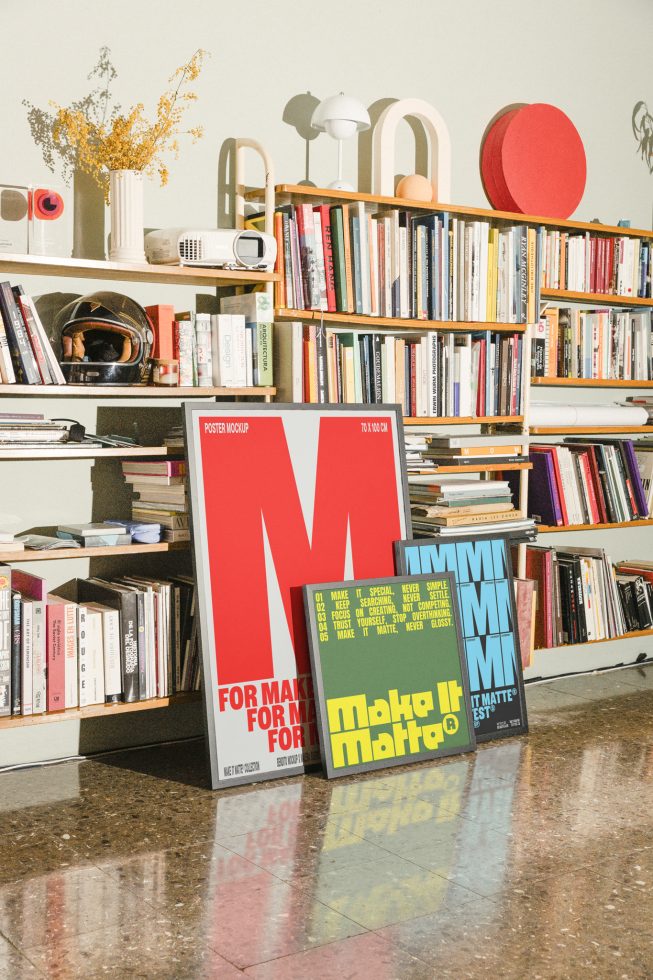 Shelf of books and decor. Three posters on floor with different designs, ideal for poster mockup templates in a creative workspace setting.