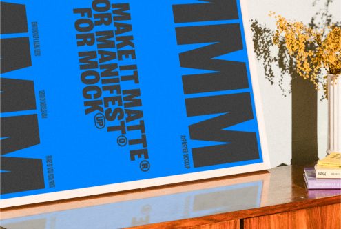 Poster mockup design featuring bold black text on blue background propped on a wooden table with decorative flowers; ideal for designers Posters Templates