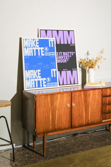 Mockups of two colorful posters displayed on a mid-century wooden cabinet with books and a vase, ideal for graphic designers seeking stylish presentation templates.