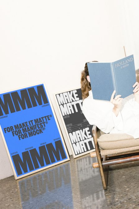 Designer reading book next to posters mockup. Blue and black minimalist poster designs. Perfect for showcasing poster designs, matte finishes, and typography.