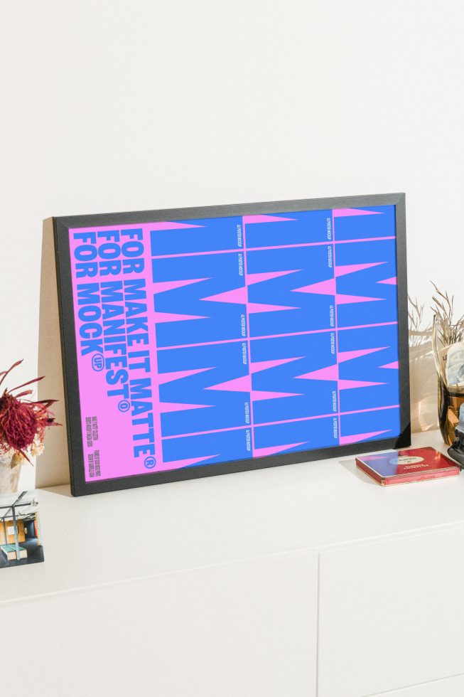 Poster mockup featuring bold pink and blue typography in a black frame on a desk. Ideal for graphic design and presentation templates for designers.