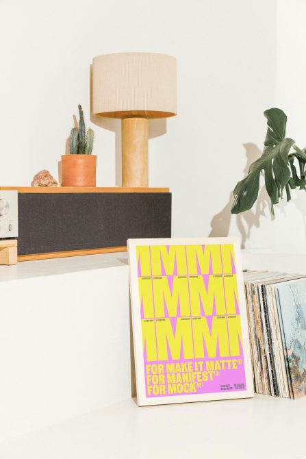 Poster mockup featuring vibrant yellow and pink text leaning on a shelf with a lamp, cactus, and vinyl records in the background. Perfect for designers.