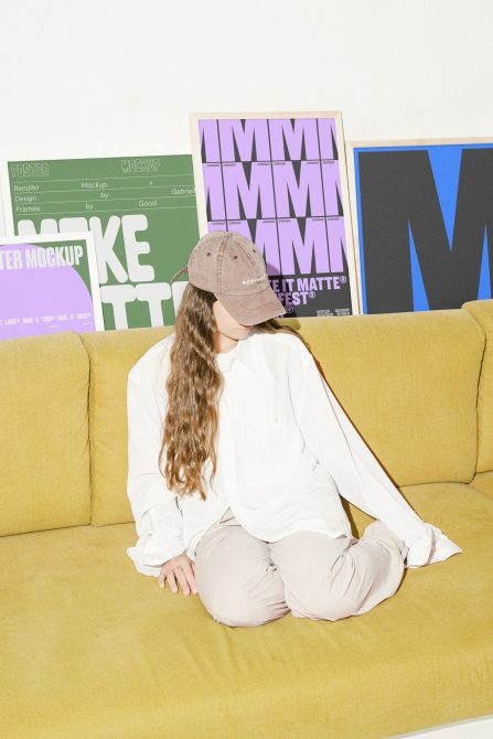 A designer sitting on a yellow couch with poster mockups behind them. Keywords: poster mockup, design, template, graphics, digital assets for designers.