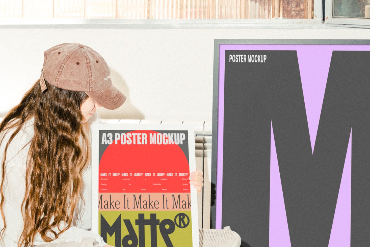 Designer with long hair and cap holding A3 poster mockup in a bright room. Multiple colorful posters visible. Perfect scene for mockups and templates.