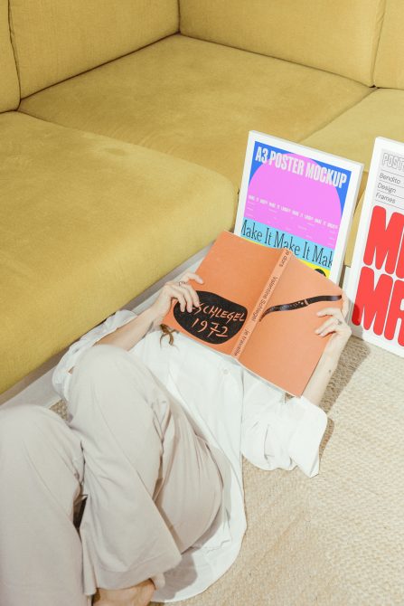 A designer lying on the floor with an open book, surrounded by colorful A3 poster mockups, ideal for showcasing graphic design templates and poster presentations.