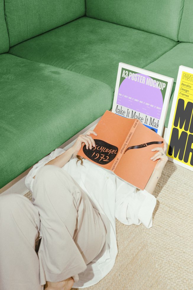 Woman reading book on floor near green sofa with A3 poster mockups. Perfect for design showcase, templates, and mockups collection. Ideal for graphic designers.