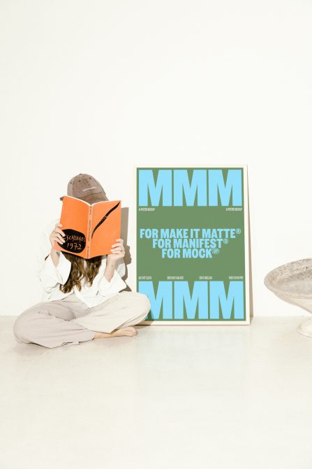 Poster mockup with large MMM text on green background beside a person reading a book. Ideal for designers. Keywords: poster mockup, design asset, graphic template.