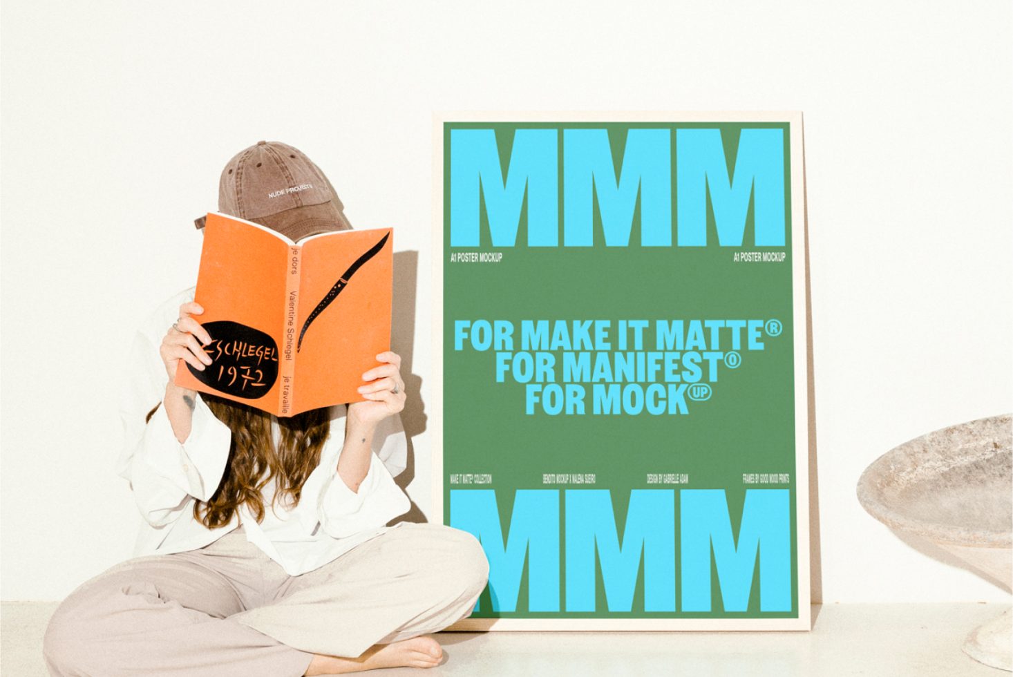 A person in relaxed attire sits holding a book obscuring their face next to an A1 poster mockup with bold typography. Ideal for designers creating poster presentations.