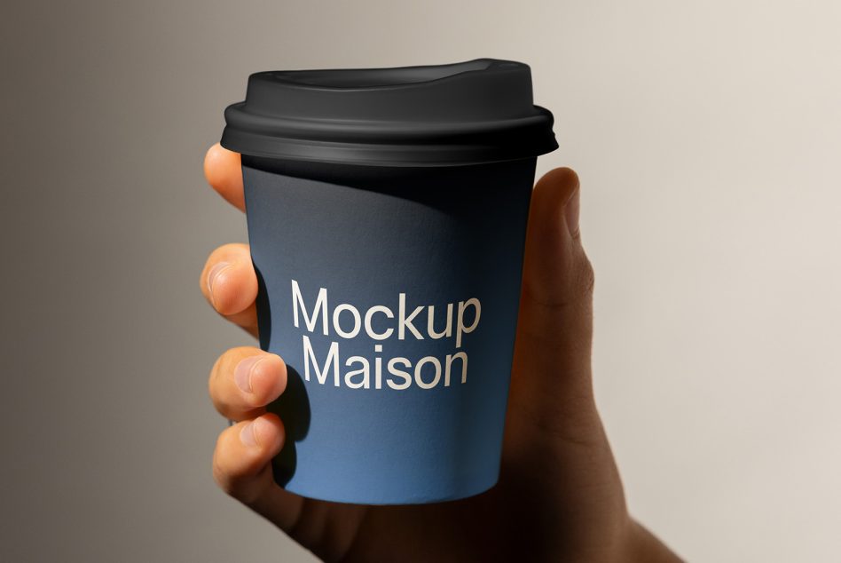 Hand holding dark blue coffee cup with black lid, white text reads "Mockup Maison"