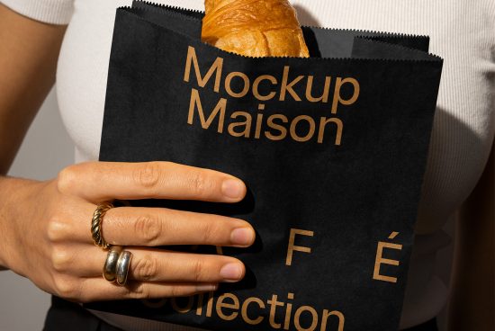 Black paper packaging mockup featuring a hand holding it with a croissant inside. Perfect for showcasing cafe branding. Ideal for designer templates and mockups.