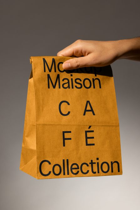 Designer hand holding a brown paper bag with bold black text Mockup Maison Cafe Collection ideal for packaging mockups and branding design projects