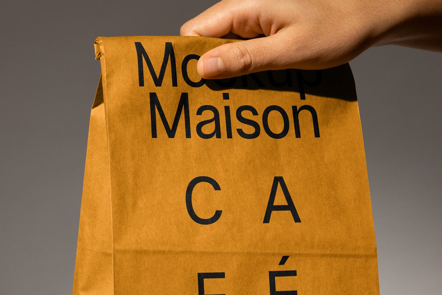 Hand holding a brown paper bag with bold black text used for a mockup design. Ideal for designers needing packaging mockups. SEO keywords: Mockup, Packaging, Design