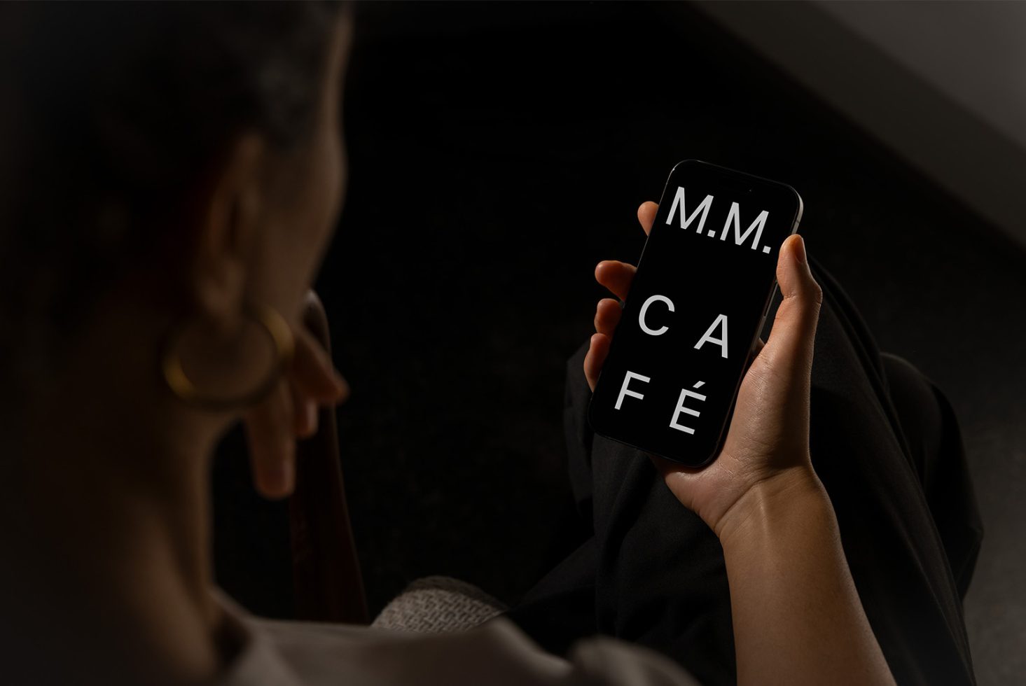 Person holding smartphone displaying modern font letters M M C A F E in dark setting, ideal for digital designers seeking sleek typography and font resources