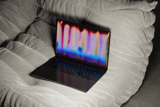 Photo of sleek black laptop on gray cushion with an abstract, colorful, digital effect on screen. Ideal for digital designs, realistic mockups, and creative projects.