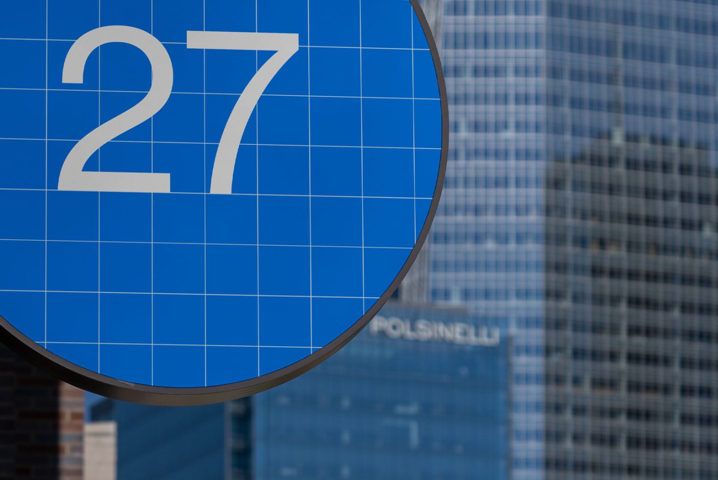 Blue grid-lined sign with the number 27 against a city skyscraper backdrop digital mockup signage template urban design asset for city-related projects