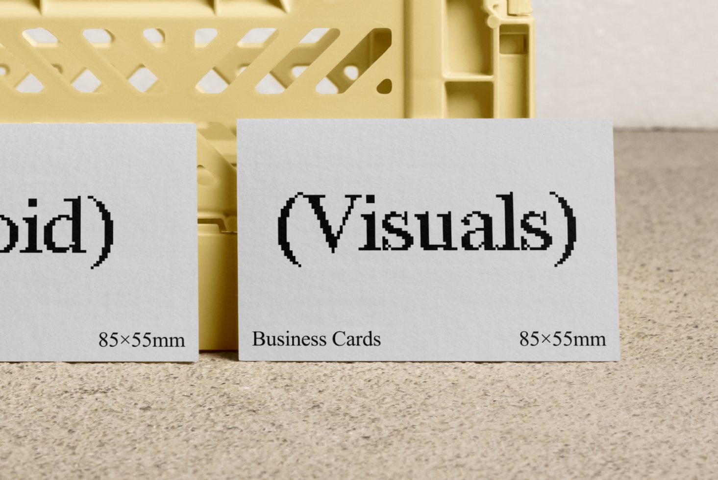 Close-up of two white business cards with pixelated text on a beige surface. Business card mockup, design assets, templates for designers, 85x55mm size.