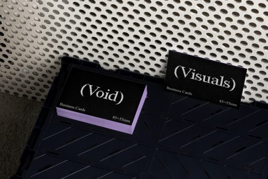 Stack of black business cards with a textured white font reading Void and Visuals on a dark industrial surface with perforated metal background. Templates Mockups