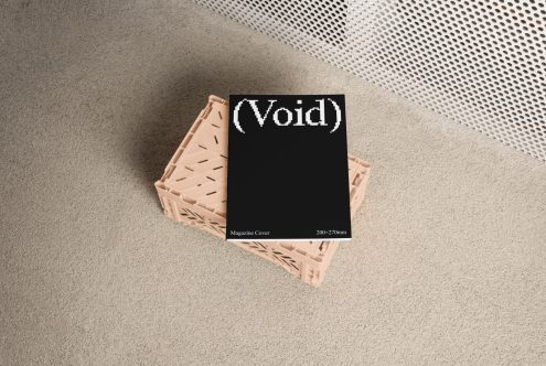 Magazine cover mockup featuring a black cover with Void text in a pixelated font lying on a beige crate on a carpeted floor. Perfect for design presentations.