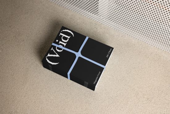 Stack of black magazines with a minimalist cover design, bound with a blue strap, placed on a beige carpet floor near a perforated white partition.