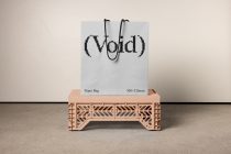 Light blue paper bag with black handles showing pixelated void logo on wooden crate