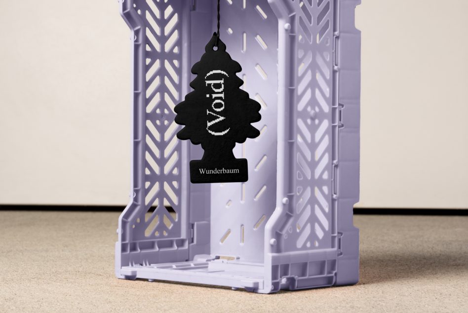 Black tree-shaped air freshener reading Void hanging in light purple plastic crate on beige surface suitable for graphics design mockup or template.