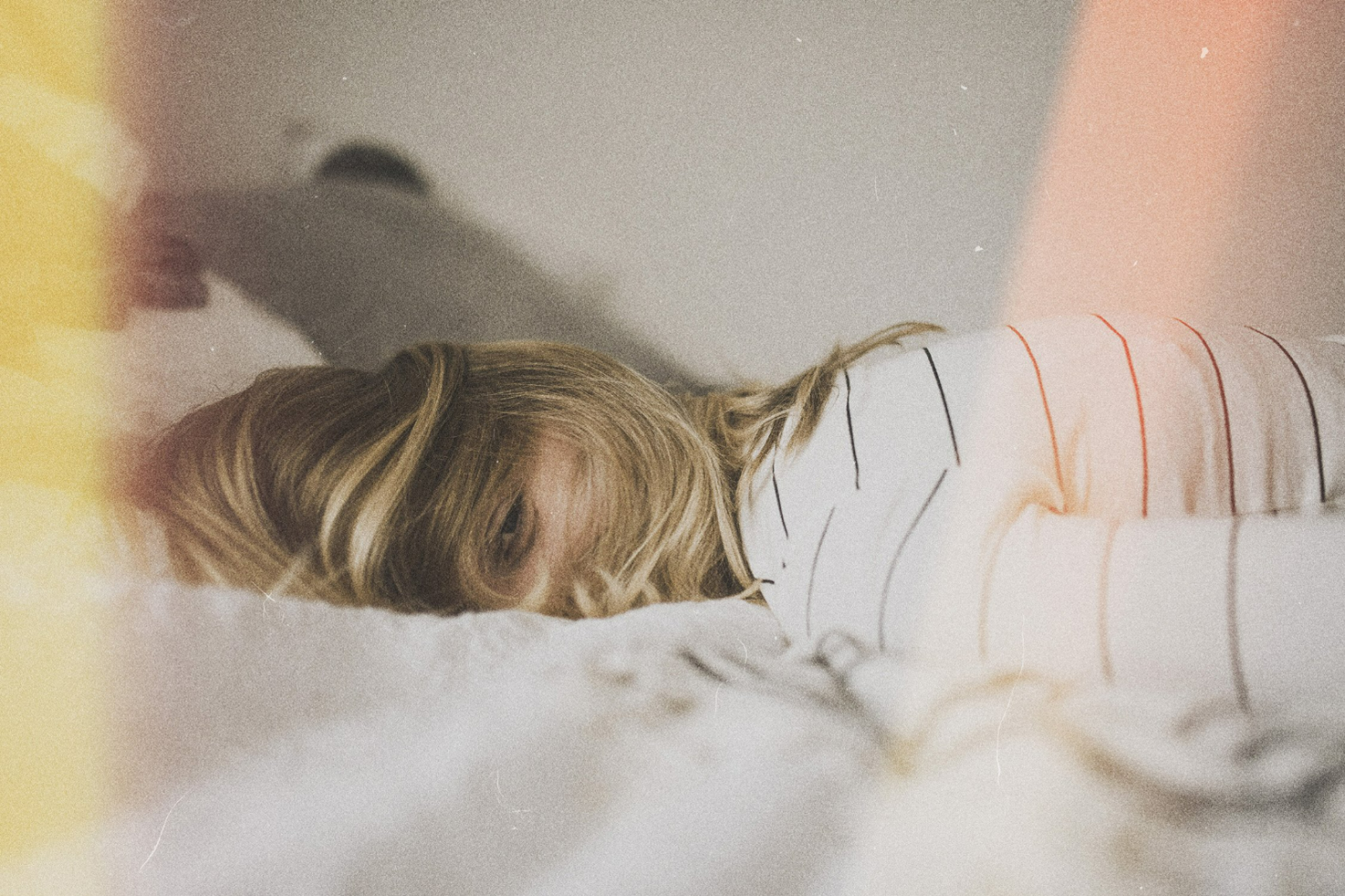 Vintage photo effect of a woman lying on a bed wearing a striped shirt. Retro aesthetic, soft light, and grainy texture. Ideal for graphic design, templates.