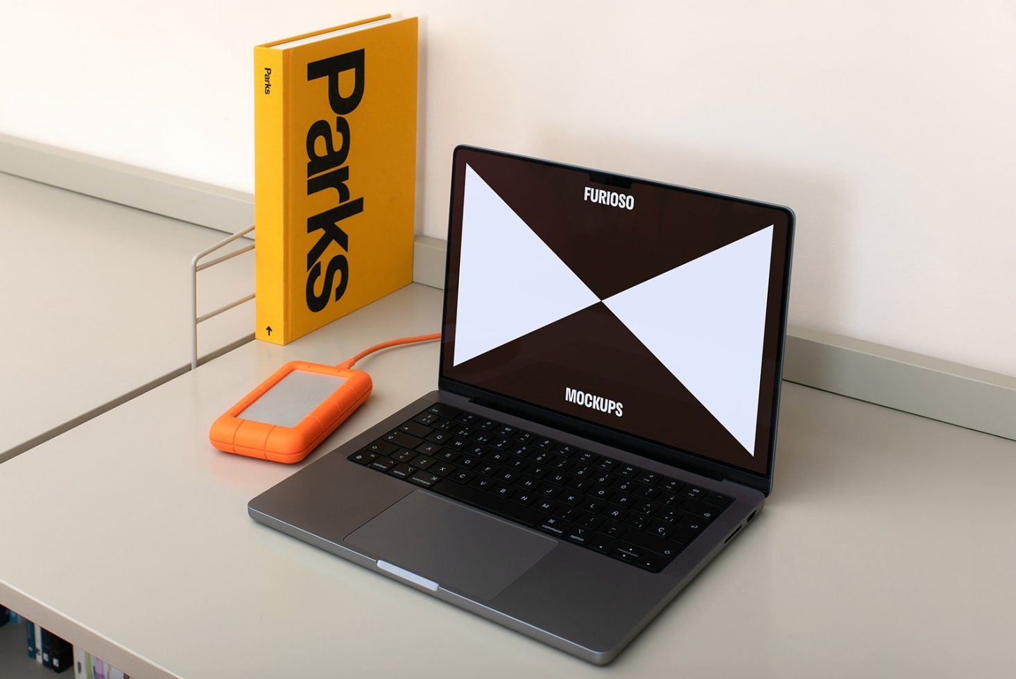 Laptop on desk displaying Furioso Mockups with orange external drive and yellow Parks book. Perfect for designers looking for high-quality laptop screen mockups.