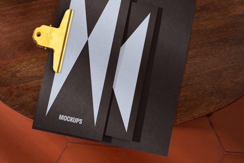 Black folder and papers with geometric designs on a wood table, labeled mockups. Gold clip at the top, suitable for showcasing branding or design presentations