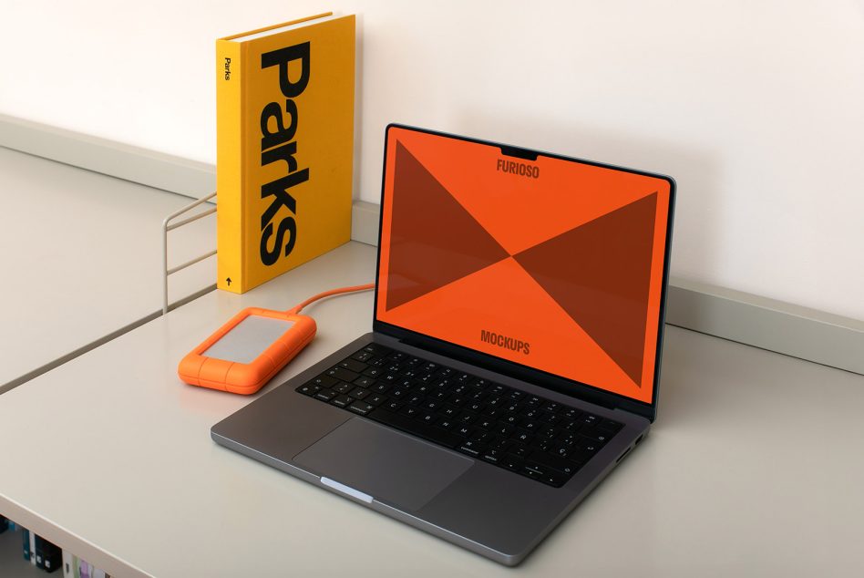 Laptop mockup on a desk with an orange external hard drive and a yellow book labeled Parks in the background perfect for designers showcasing technology graphics